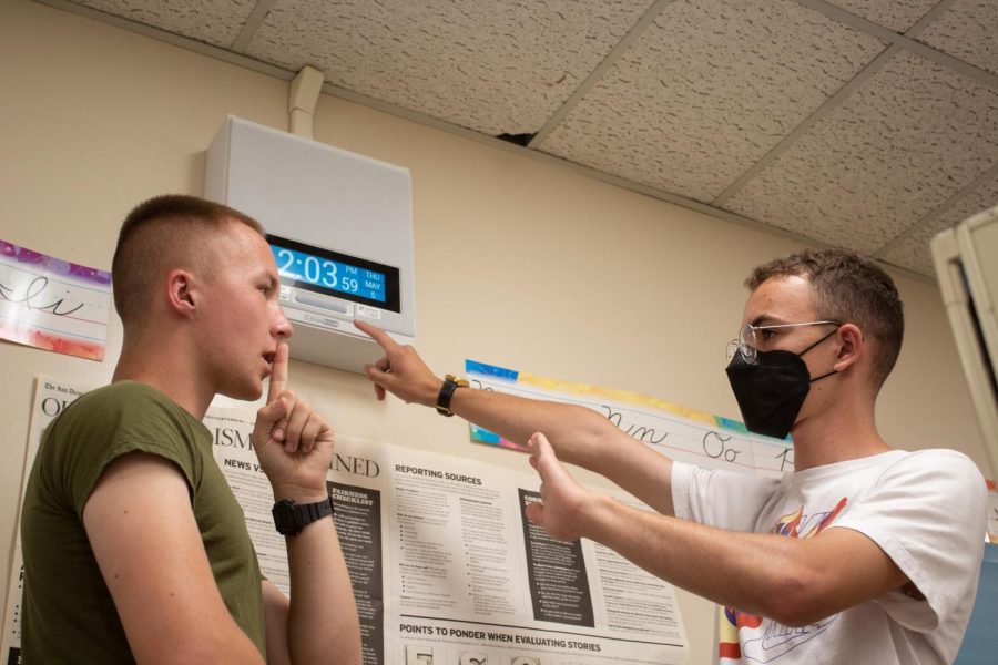 Senior Maximilian Nelson and Junior Shaynen Gold stand in front of a clock/intercom.